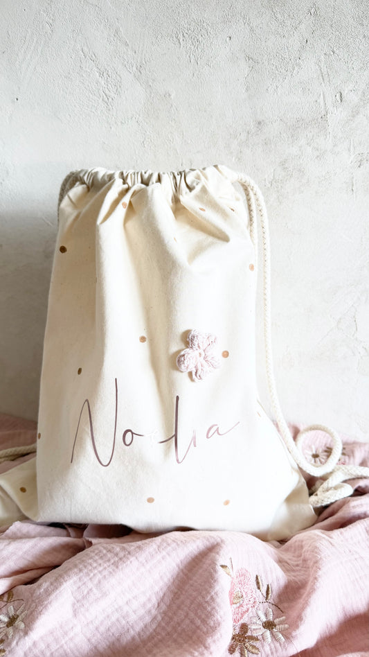 Personalisierter Bio-Baumwoll-Turnbeutel mit rosa Metallic-Name, Häkelblume und hellbraunen Punkten