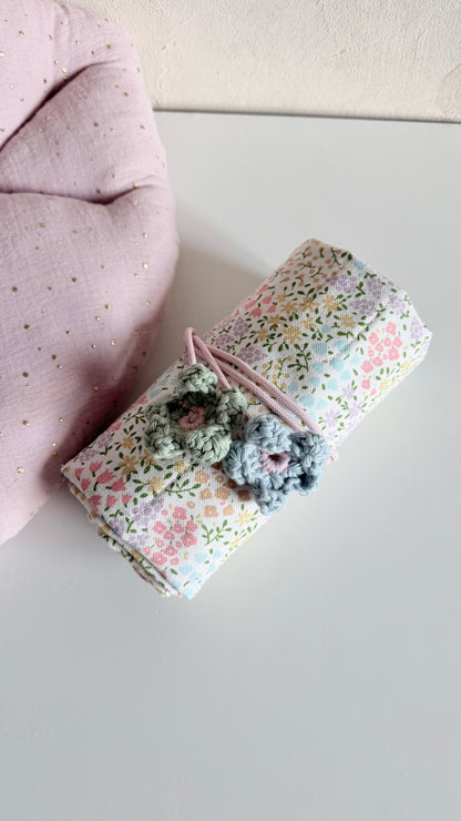 Gerolltes Blumenwiese-Mäppchen mit zwei handgehäkelten Blüten als Verschlussdetail