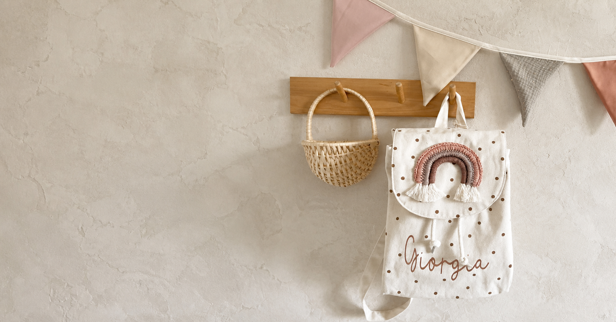 Regenbogen-Kinderrucksack mit Name im warmen Kinderzimmer im Querformat