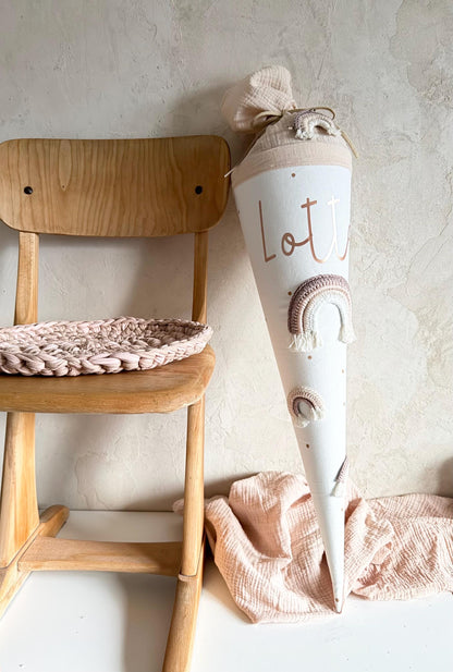 Personalisierte Regenbogen-Schultüte in Rosé und Creme am Holzstuhl
