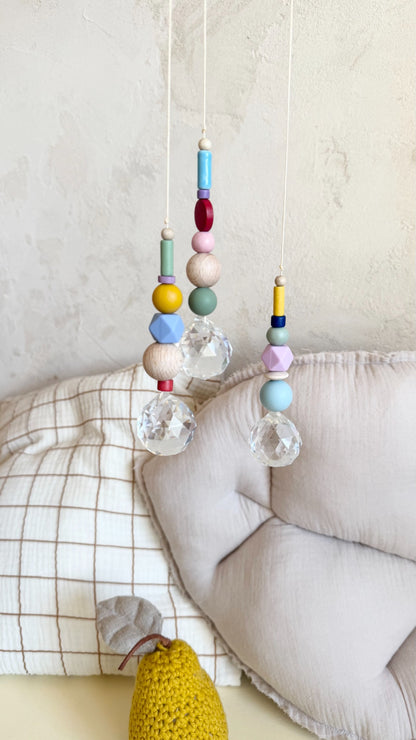 Drei bunte Suncatcher mit Holzperlen und Kristall vor Kissen